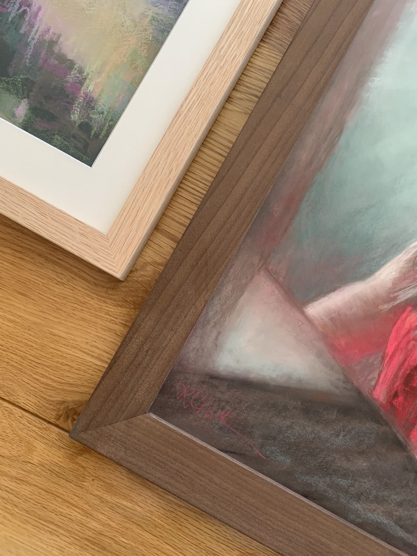 Two framed pastel paintings resting against each other, showing the mat and the moulding